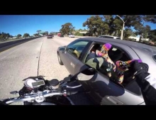 Motorcyclist grabs some feet hanging out a car window on the freeway.
