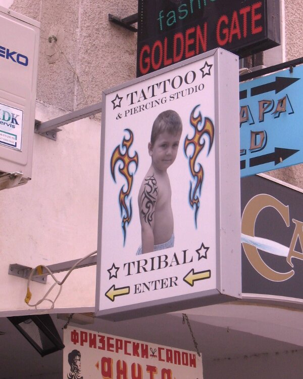 This tattoo shop sign with a kid showing off his tribal tattoo might make you say WTF!