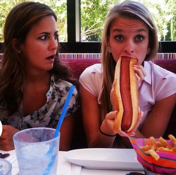 Her Friend Watches In Amazement As She Attempts To Eat A Monstrous Weenie.